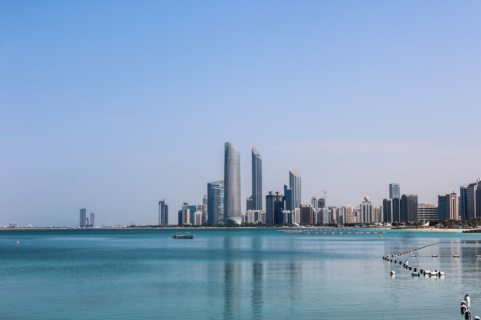 Stunning view of the Abu Dhabi skyline reflecting in the calm Gulf waters on a sunny day.