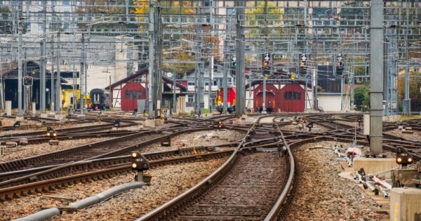 View of multiple railway tracks with signals and buildings in an urban setting during daytime.