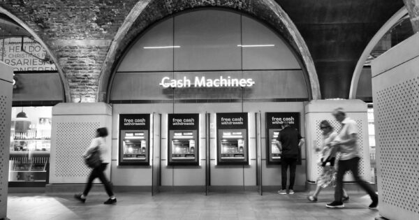 Black and white photo of people using cash machines in a metro station.
