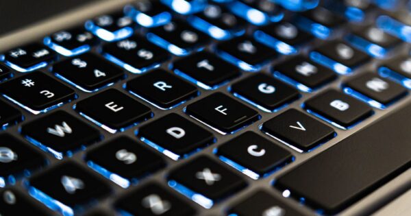 Detailed view of a backlit laptop keyboard keys with blue LED lighting for tech concepts.