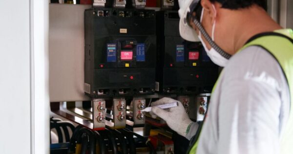 Technician wearing safety gear inspecting electrical panels in an industrial setting.