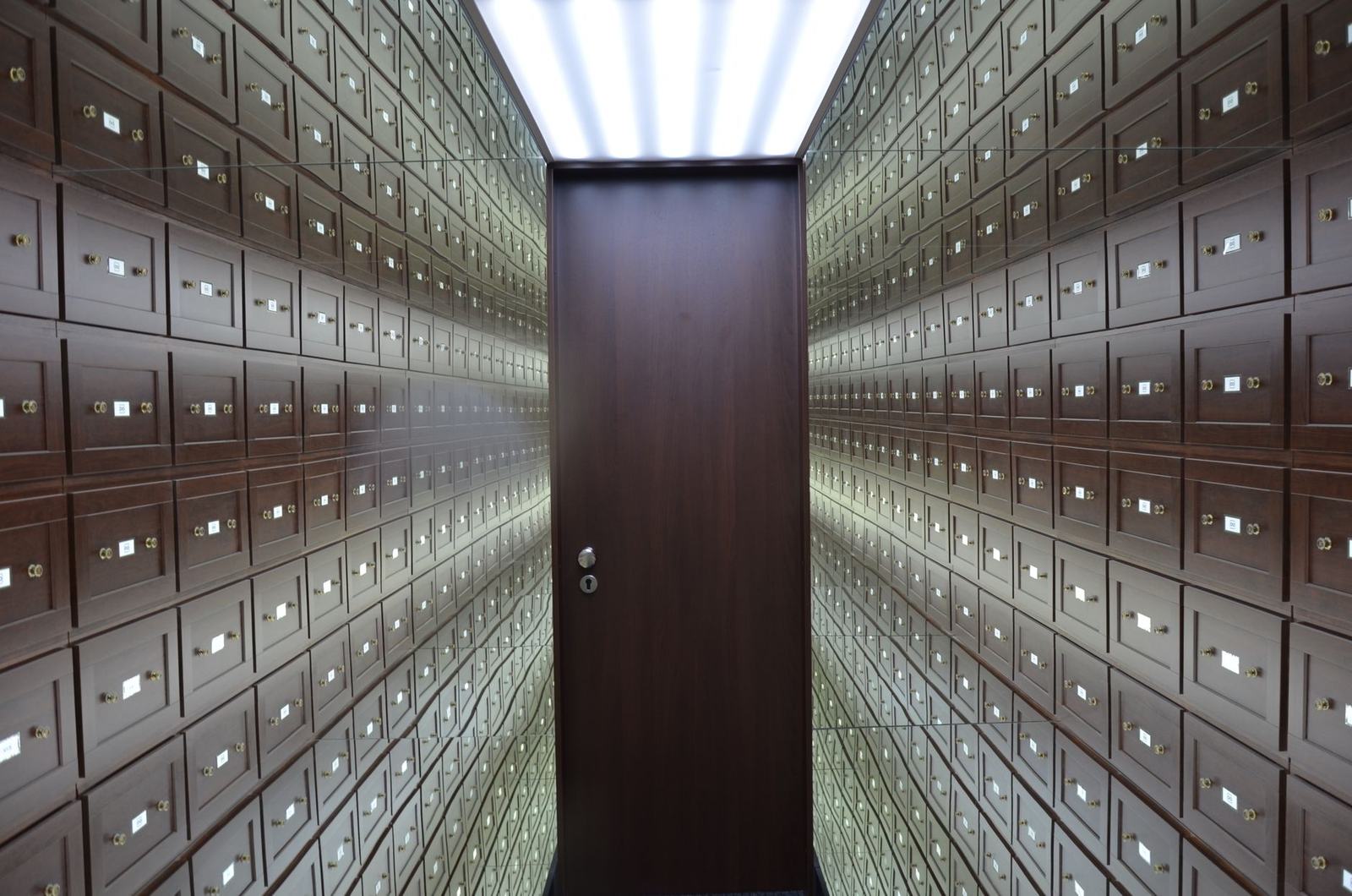 Wooden lockboxes line the walls of a modern, secure vault with a central wooden door.