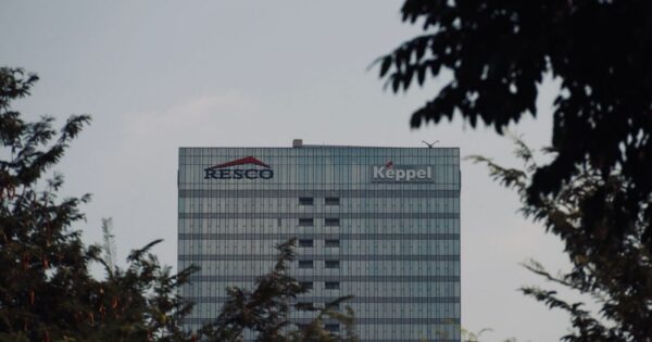 Tall modern office building with logos in an urban setting, framed by trees, during the day.