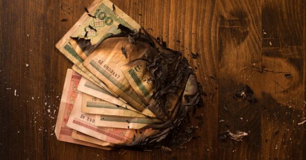 Scorched banknotes scattered on a dark wooden table, symbolizing financial loss.