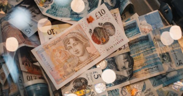 A detailed view of British £5 and £10 pound sterling notes with coins, featuring warm bokeh effects.