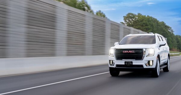 White GMC Yukon XL SUV speeding along a highway, showcasing luxury travel.