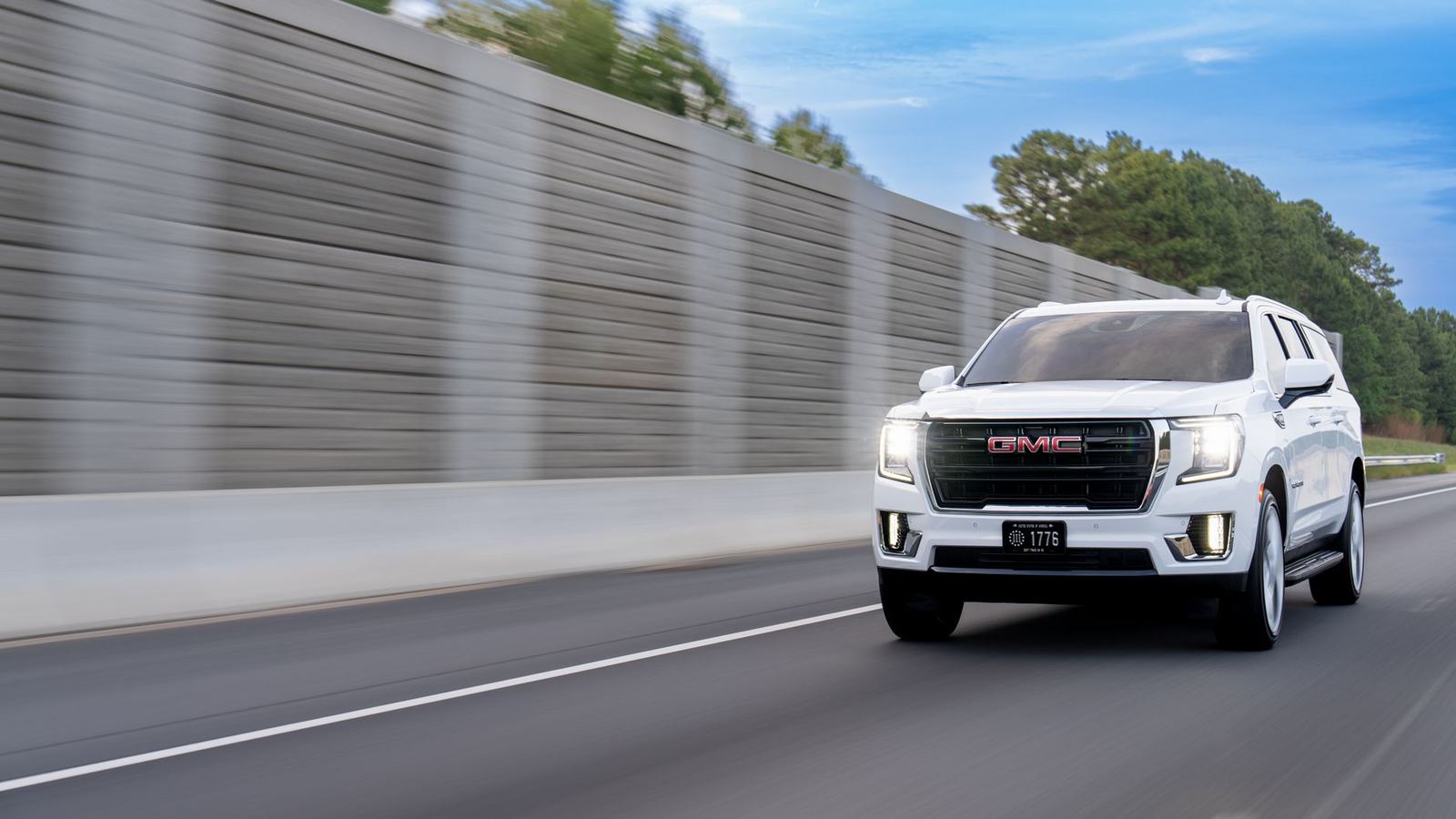 White GMC Yukon XL SUV speeding along a highway, showcasing luxury travel.