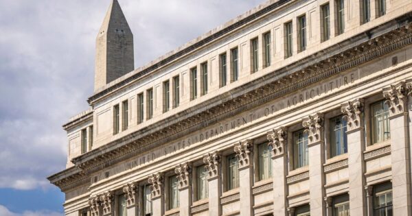 US Department of Agriculture building with Washington Monument behind, blue sky with clouds.
