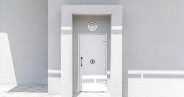 A minimalist white door set against a plain wall, casting geometric shadows in natural sunlight.