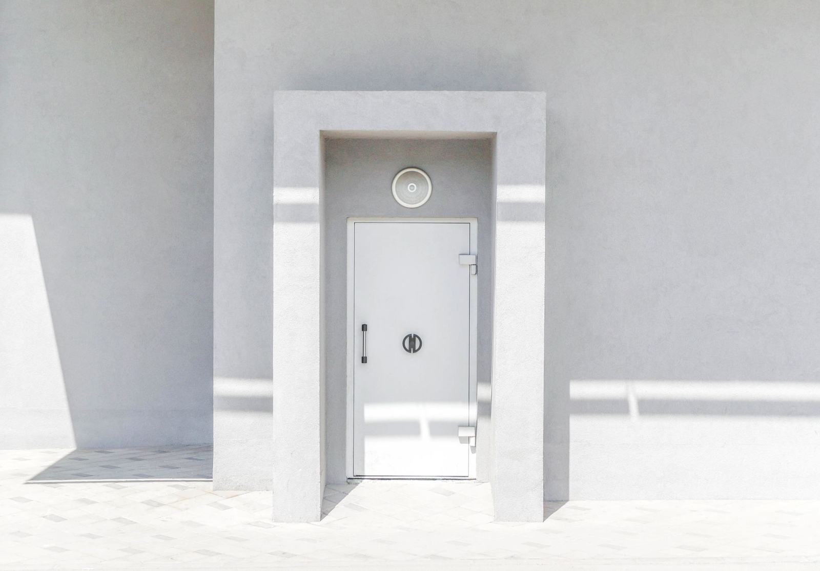 A minimalist white door set against a plain wall, casting geometric shadows in natural sunlight.