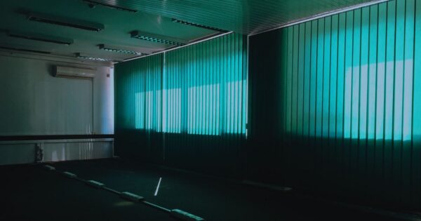 Dark empty room with vertical green blinds and natural light filtering through.