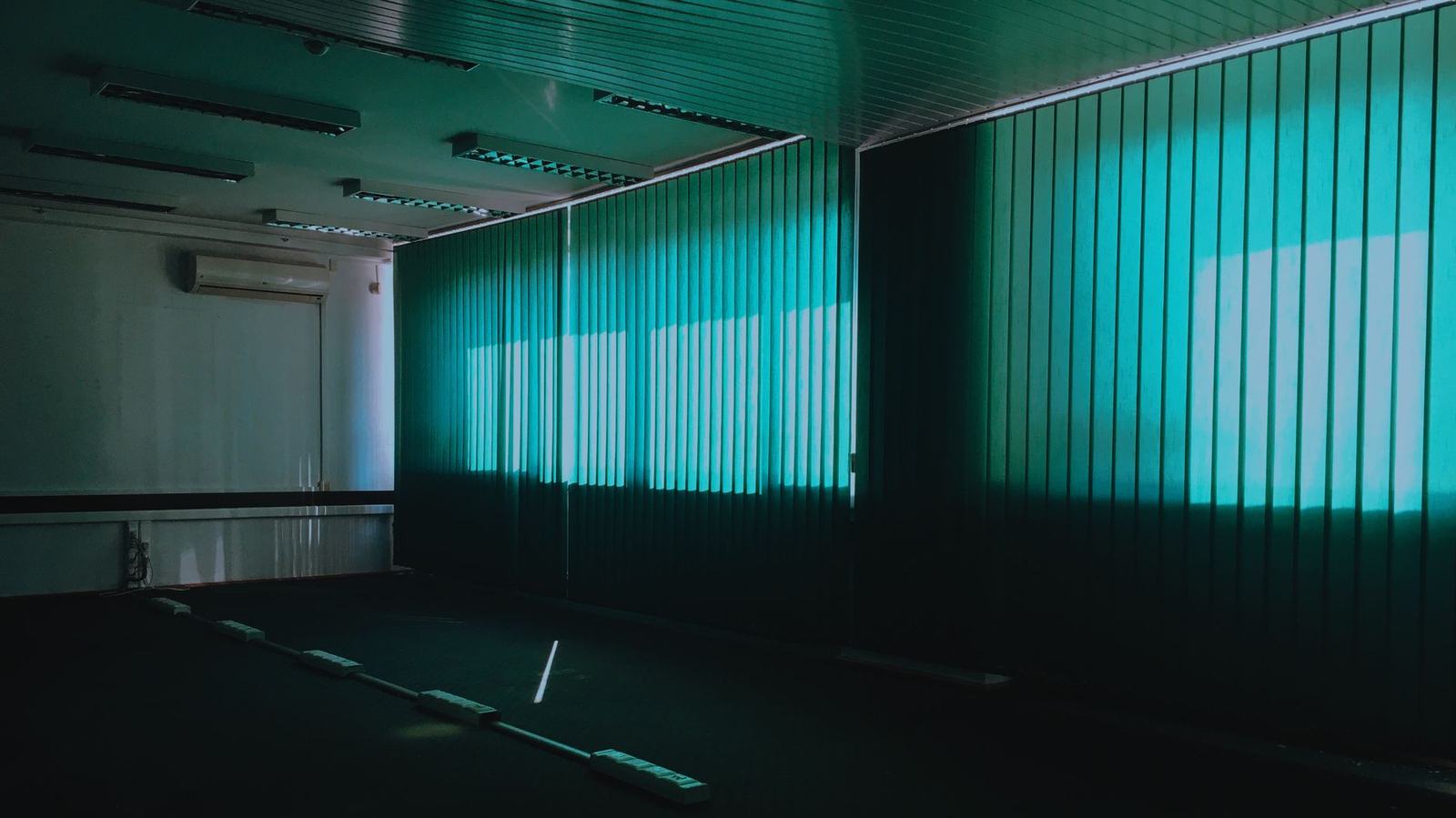 Dark empty room with vertical green blinds and natural light filtering through.