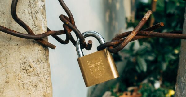 A brass padlock securing a rusty wire on a concrete post, symbolizing security and protection.