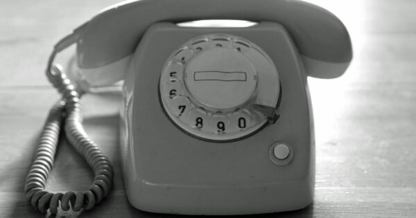 High contrast black and white image of a vintage rotary phone on a wooden surface emphasizing nostalgic communication.