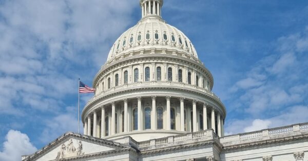A striking view of the US Capitol dome with flag and blue sky in Washington, DC.