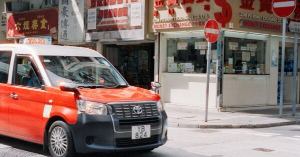 Red taxi drives past shops on city street
