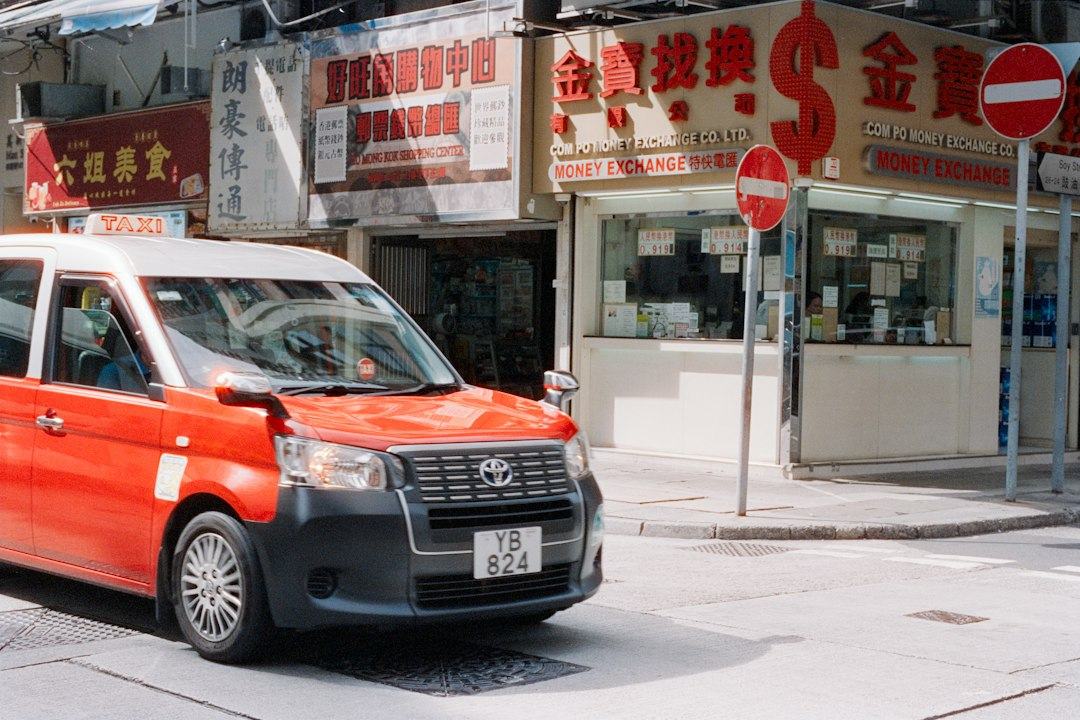 Red taxi drives past shops on city street