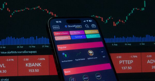 Close-up of a smartphone displaying a stock trading app against a backdrop of market charts.