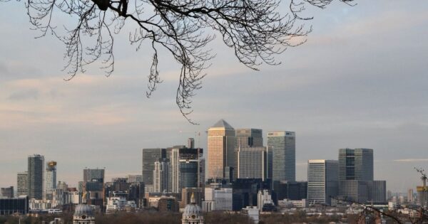 View of Canary Wharf skyline in London at dusk, framed by tree branches.