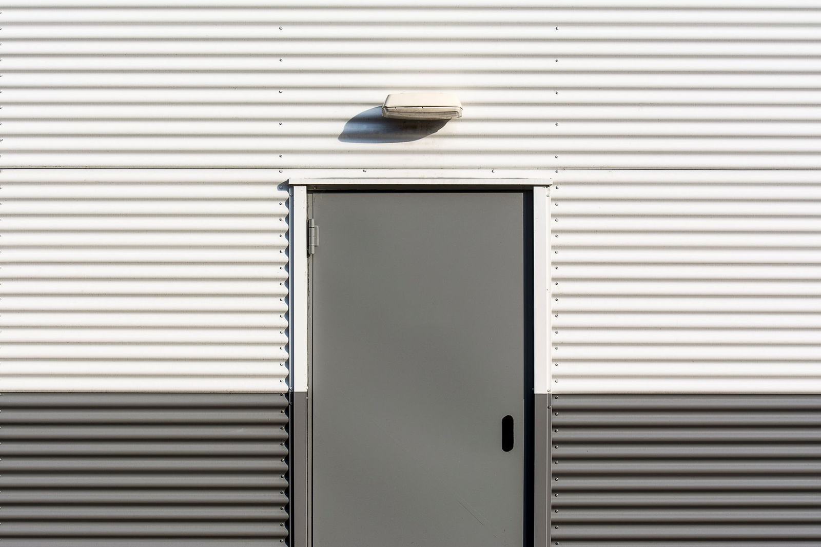 Minimalist image of a corrugated metal wall with a centered door, showcasing industrial architecture.