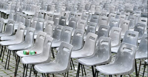 Rows of identical gray plastic chairs arranged outdoors on pavement.