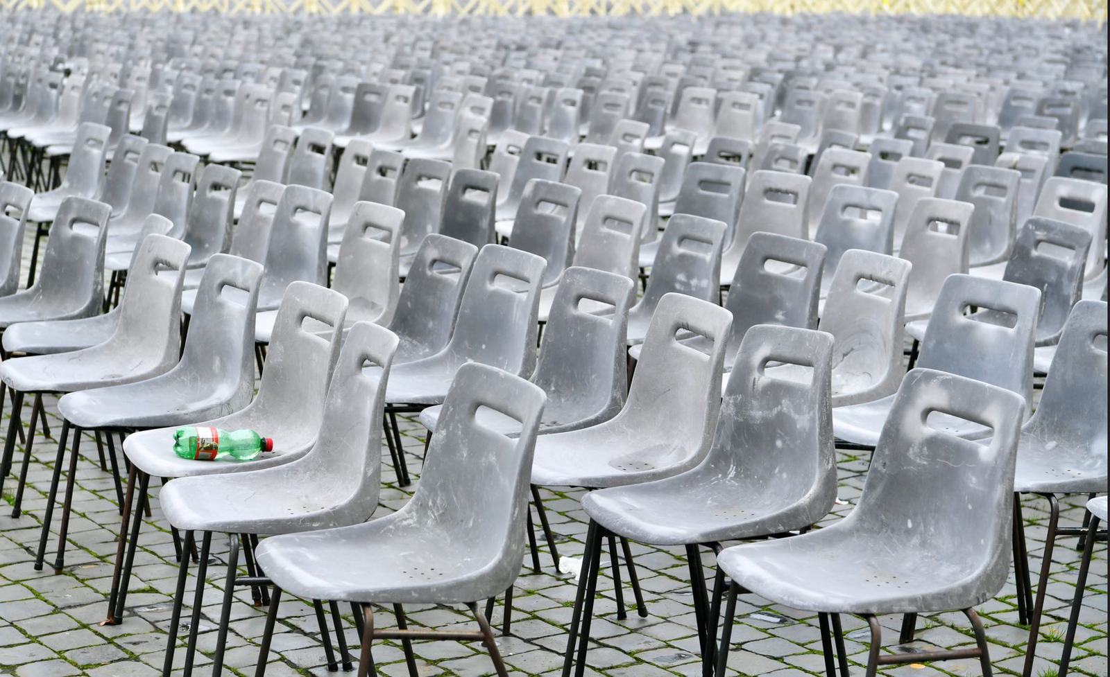 Rows of identical gray plastic chairs arranged outdoors on pavement.