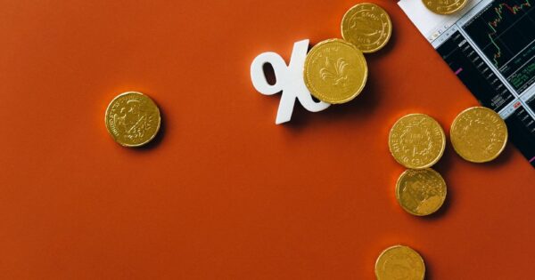 Gold coins scattered with a stock market graph and a percentage symbol on an orange background.