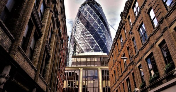 Stunning low-angle view of The Gherkin amidst historic buildings in London, showcasing architectural contrasts.