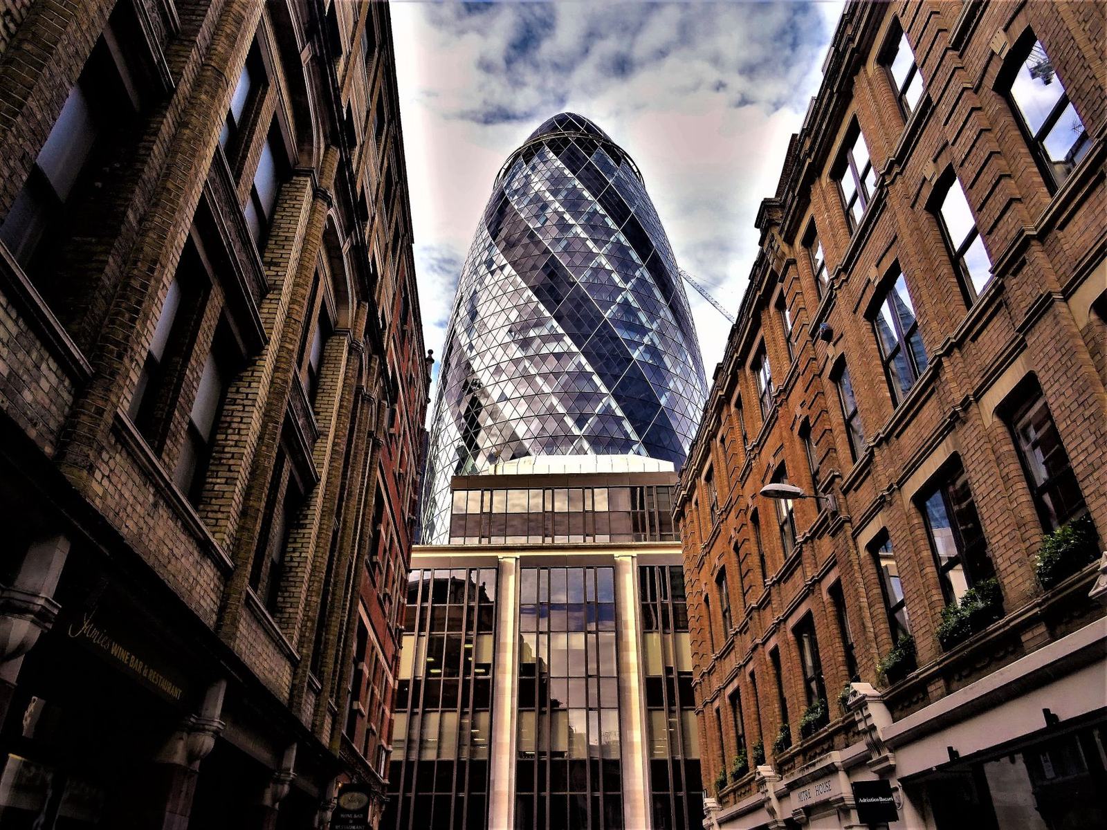 Stunning low-angle view of The Gherkin amidst historic buildings in London, showcasing architectural contrasts.