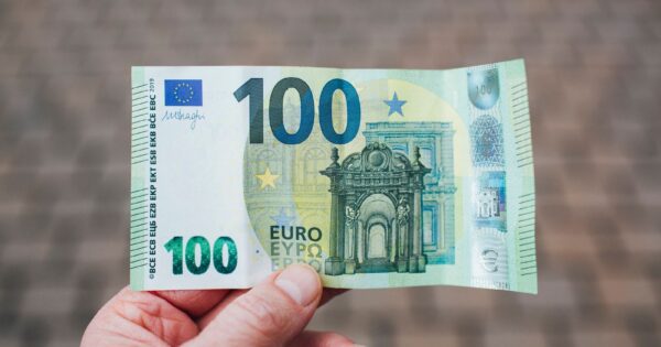 Close-up photo showing a person holding a 100 euro banknote against a blurred background.