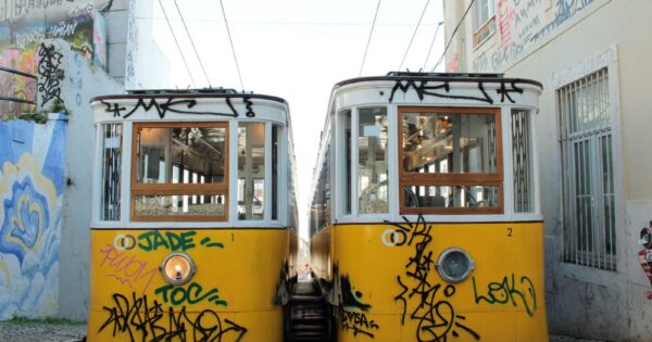 Two iconic yellow trams in a graffiti-covered street in Lisbon, Portugal. Vibrant urban scene.