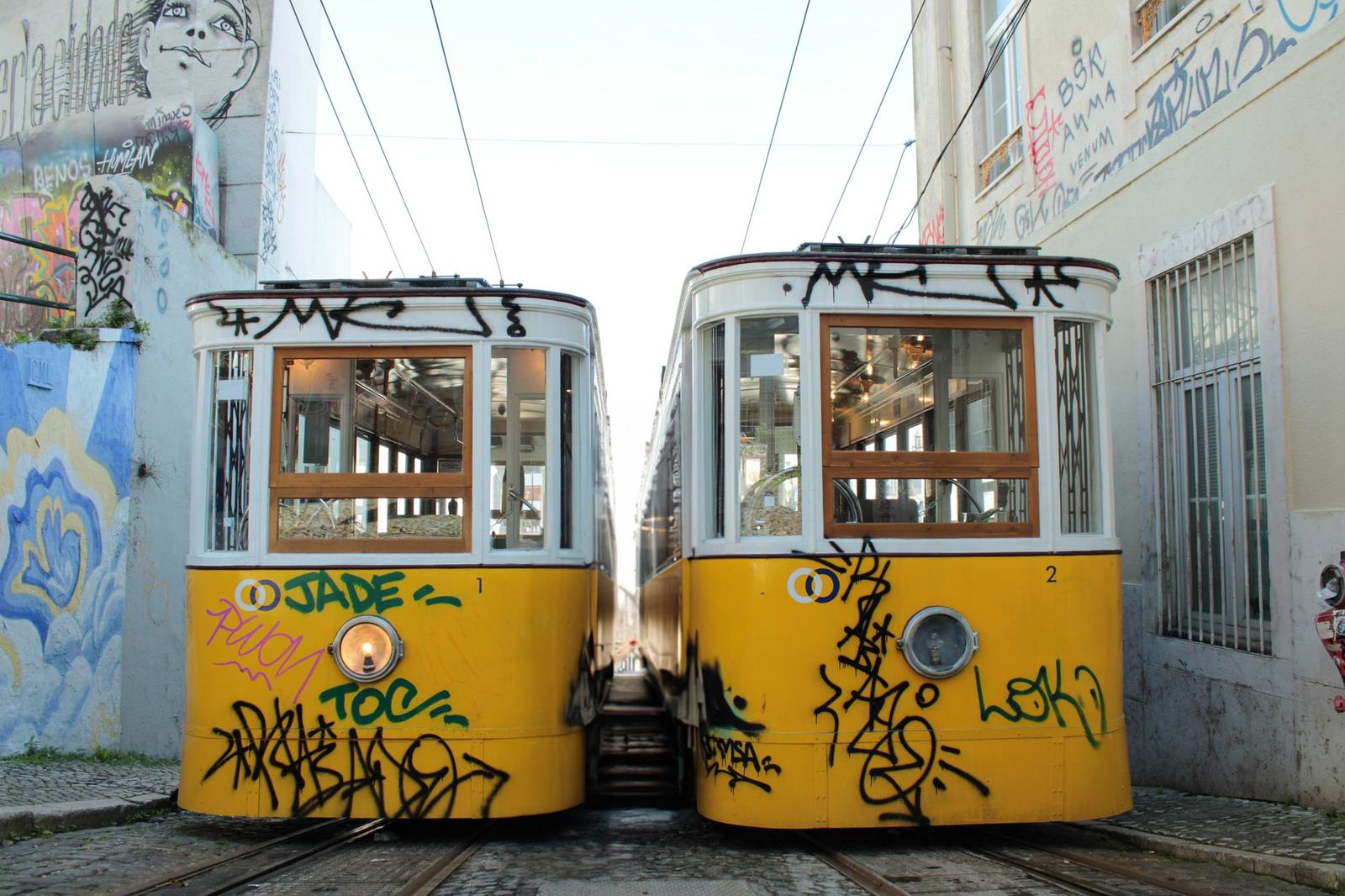 Two iconic yellow trams in a graffiti-covered street in Lisbon, Portugal. Vibrant urban scene.