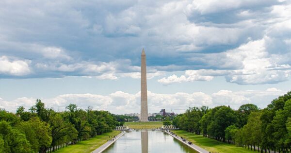 A scenic view of the Washington Monument in Washington, D.C., with reflections in the reflecting pool and a cloudy sky overhead.