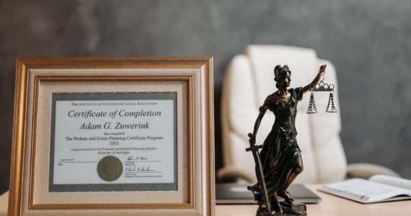 A framed legal certificate and Lady Justice figurine on a desk in a law office setting.