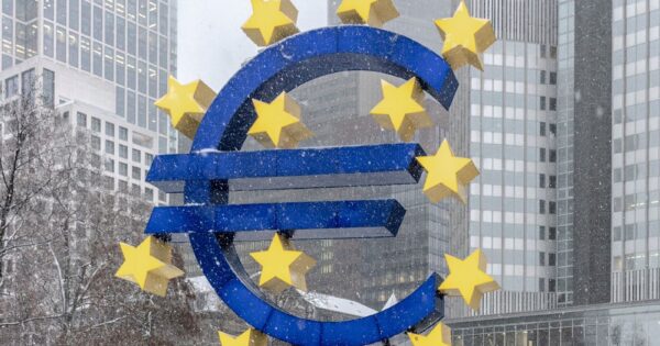 The iconic Euro symbol stands prominently amidst snowy Frankfurt skyscrapers.