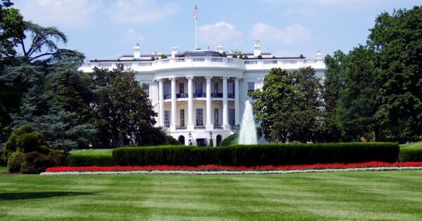 Iconic view of the White House with lush gardens and a central fountain on a sunny day.