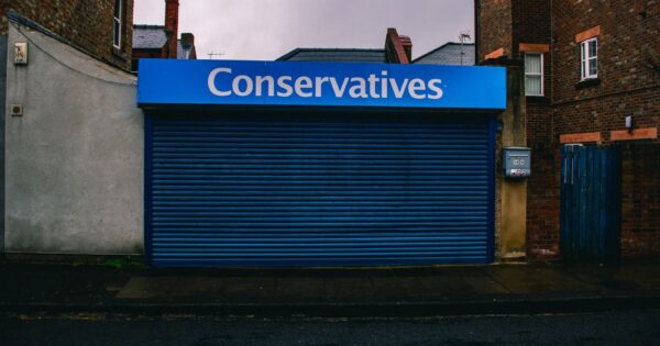 A blue closed shopfront with 'Conservatives' signage on a quiet urban street.