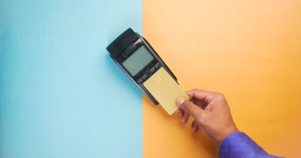 A hand tapping a credit card on a payment terminal for a contactless transaction.
