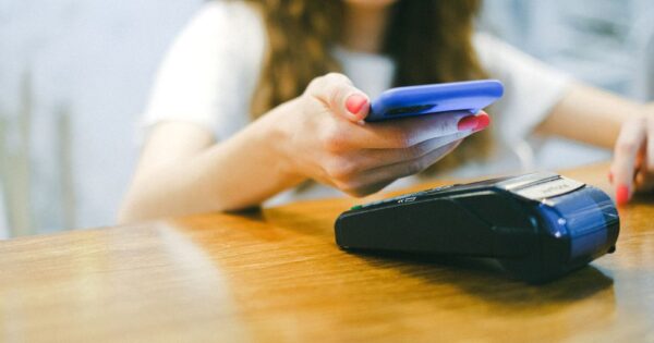 A woman processes a contactless payment using her smartphone at a payment terminal.