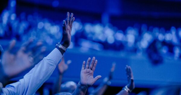 A vibrant concert audience captured with hands raised under dramatic blue lighting.
