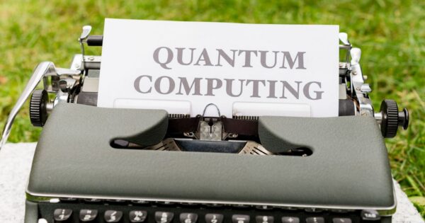 A typewriter with 'Quantum Computing' text outdoors on grass, blending old and new technologies.