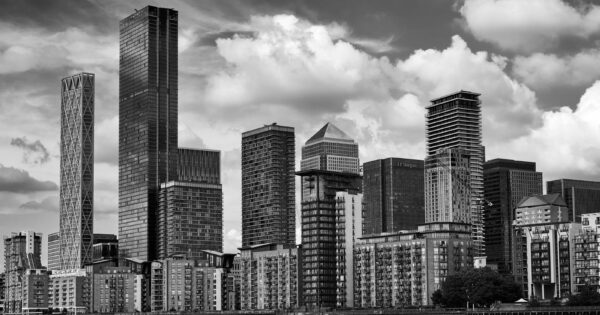 Black and white cityscape of London's iconic Canary Wharf under a cloudy sky.